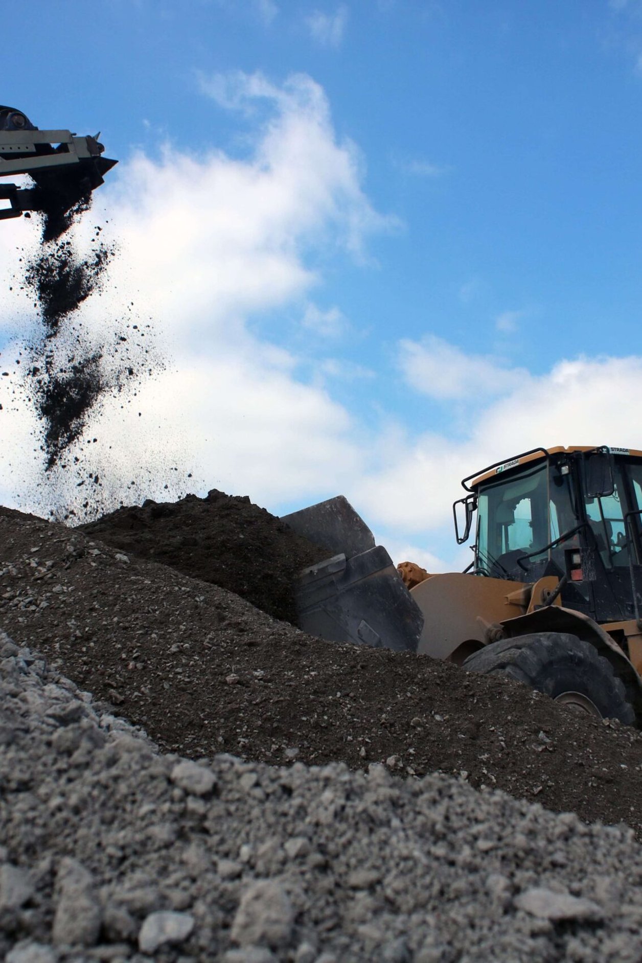 a large digger climbs up a mountain of rubble